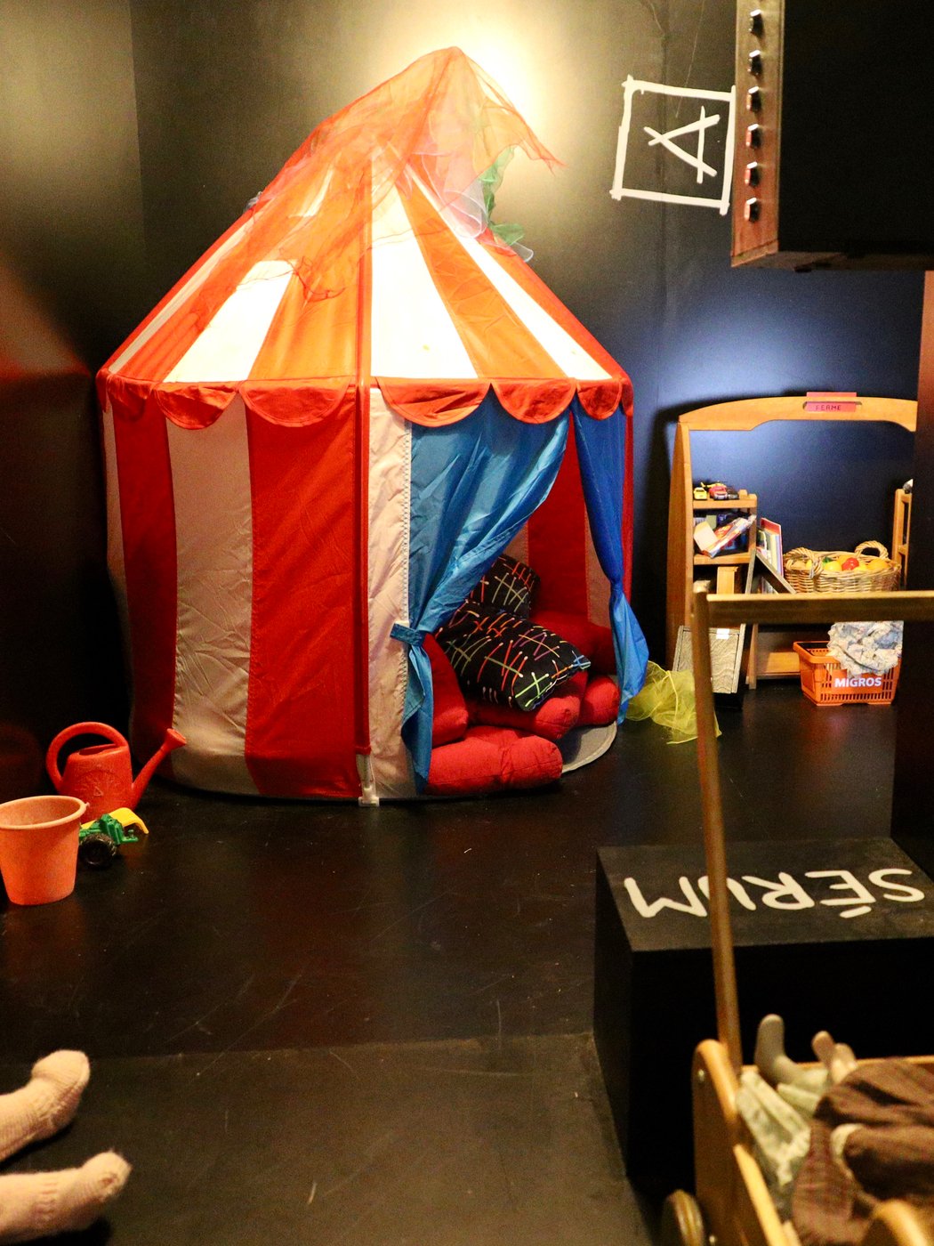Intérieur de la room terminée : tente de cirque rouge et blanche, jouets et poupées dans une pièce peinte en noir